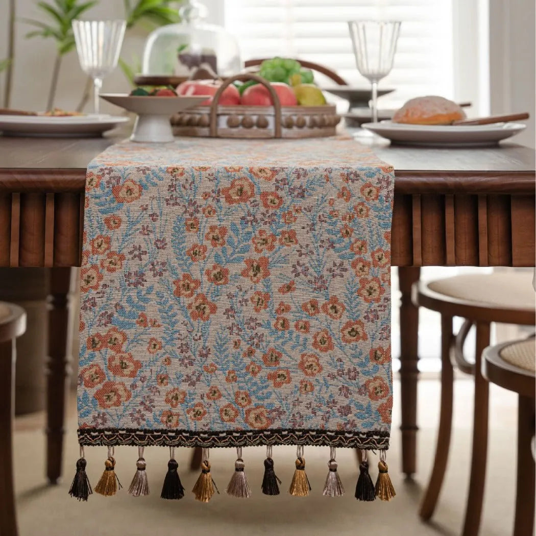 Beige jacquard table runner with floral pattern and long tassels draped over a wooden wedding table.