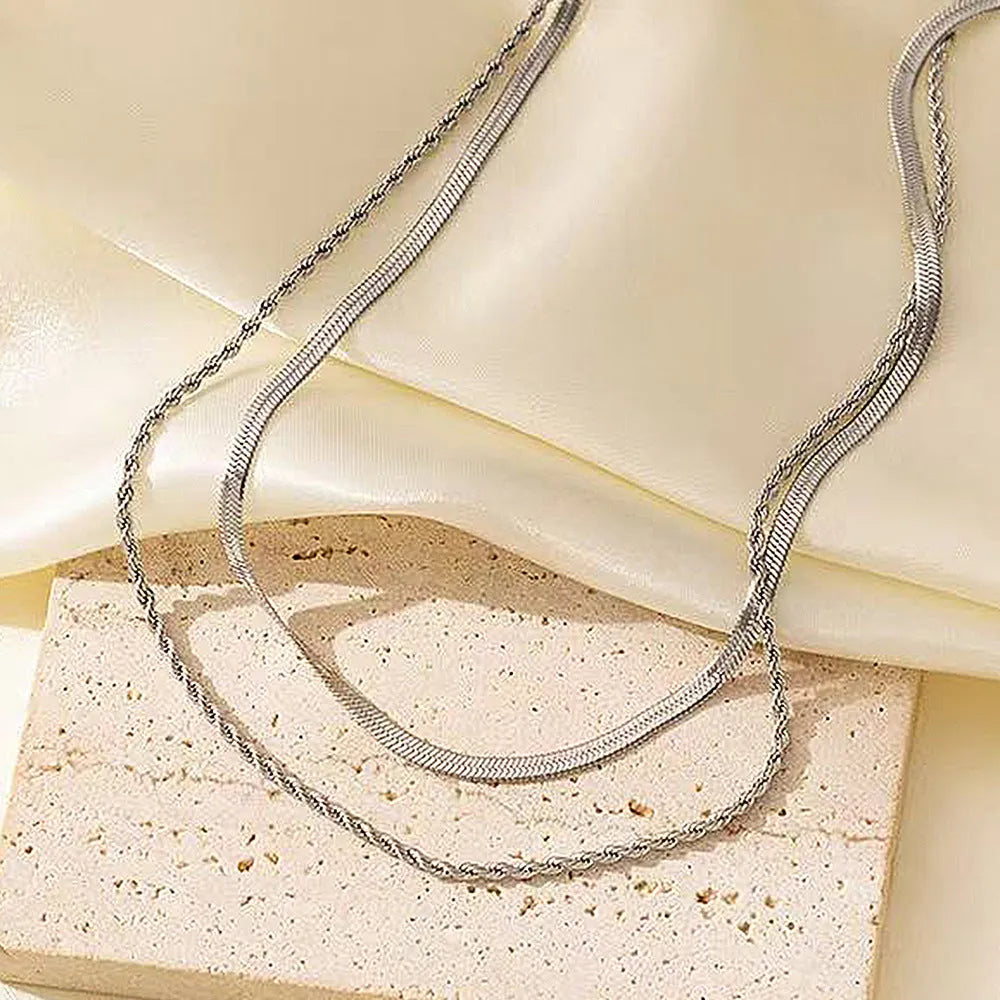 Women's silver geometric twist pendant necklace on adjustable snake bone chain against grey background.