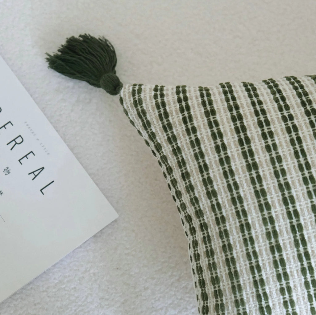 Green striped and botanical pattern decorative pillow with tassels on a bed.