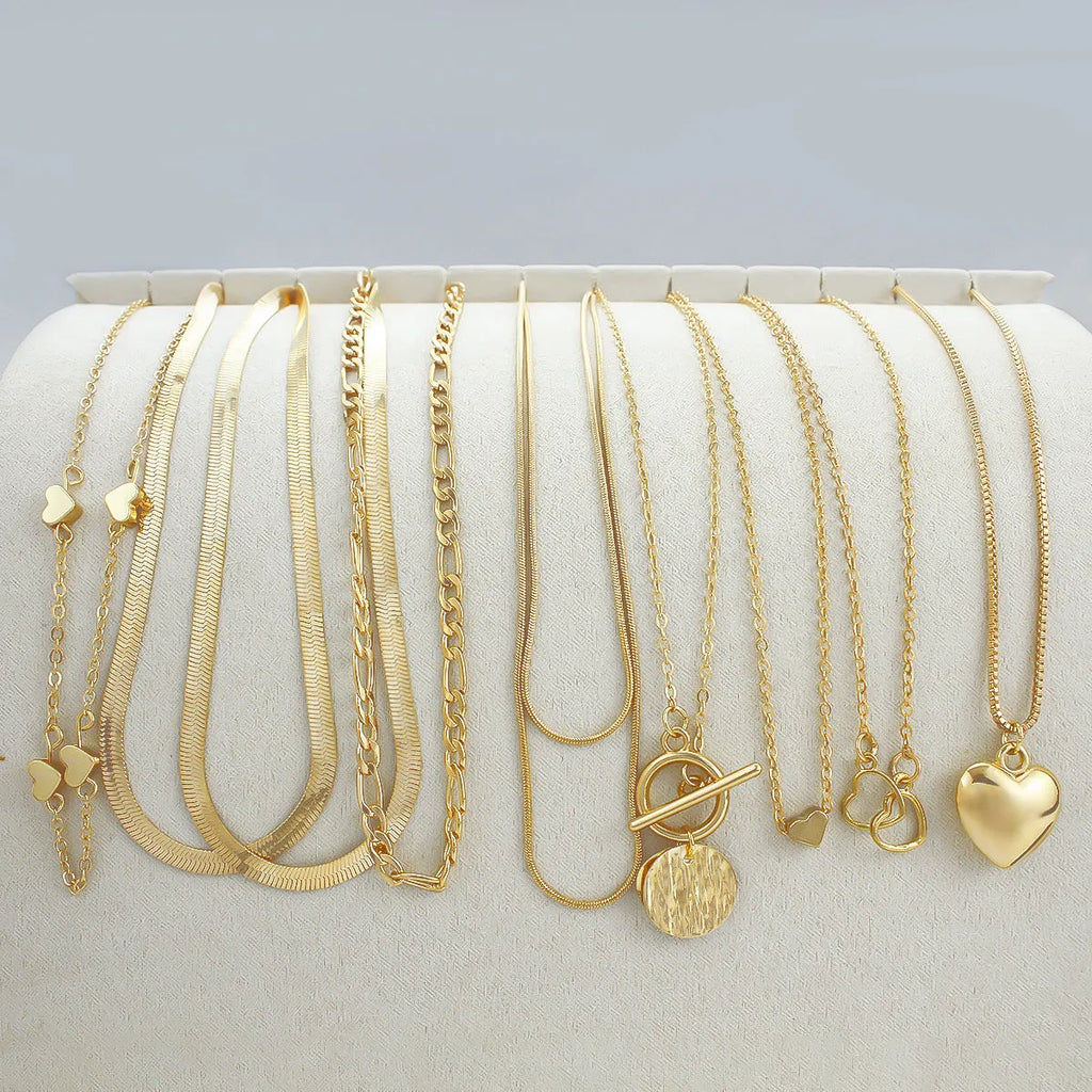 Set of ten gold-coloured women's necklaces with snake bone chains and alloy pendants on a white background.