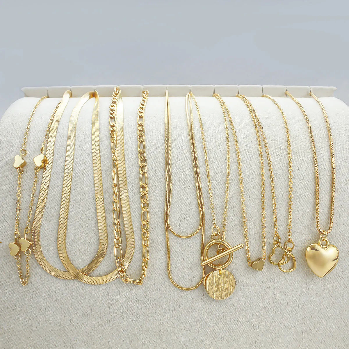 Set of ten gold-coloured women's necklaces with snake bone chains and alloy pendants on a white background.