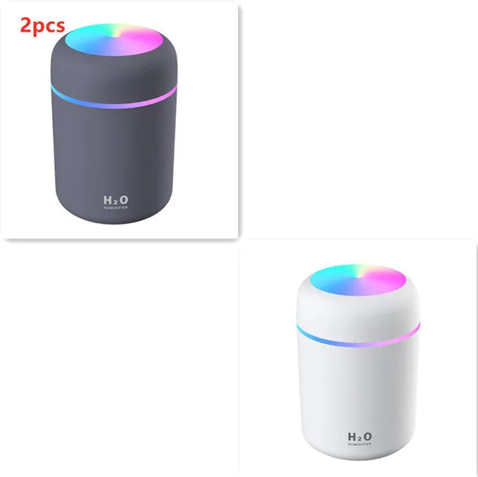 Pink USB mini humidifier with LED lights on wooden desk beside laptop