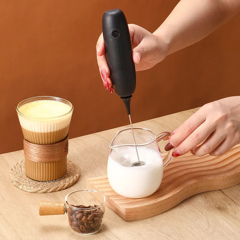 A handheld electric milk frother in black and white colours on a kitchen counter.