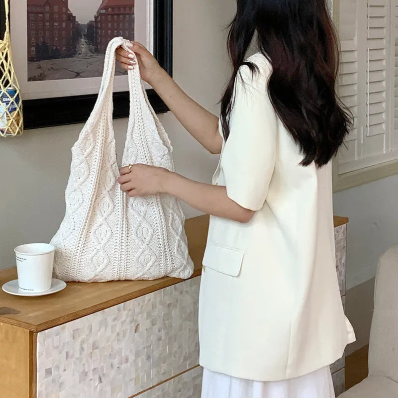 GWomens beige knitted tote bag with double shoulder straps on a wooden table.