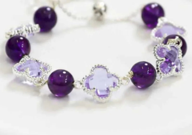 Women's artificial amethyst bracelet with four-leaf clover charm and pearl accents on a wrist.