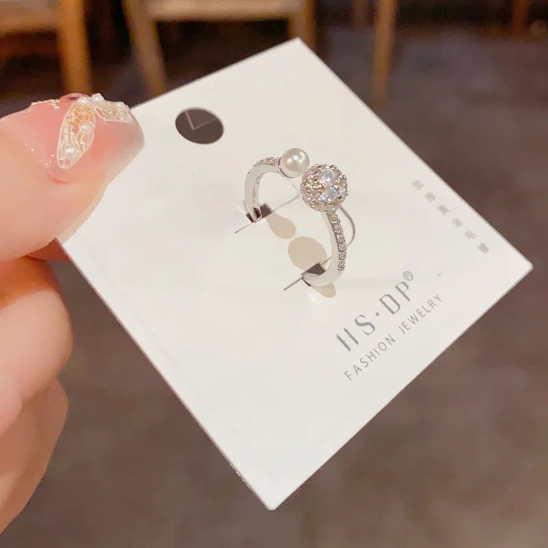 Gold or silver coloured open-end ring with a round zircon pearl on a geometric band.