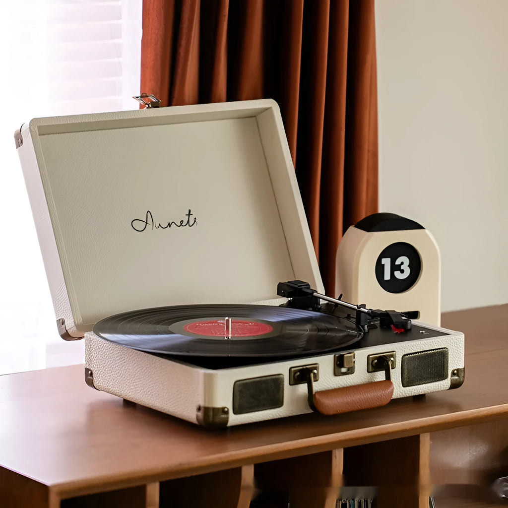 Cream-coloured retro phonograph in leather-effect suitcase with record on turntable and handle visible