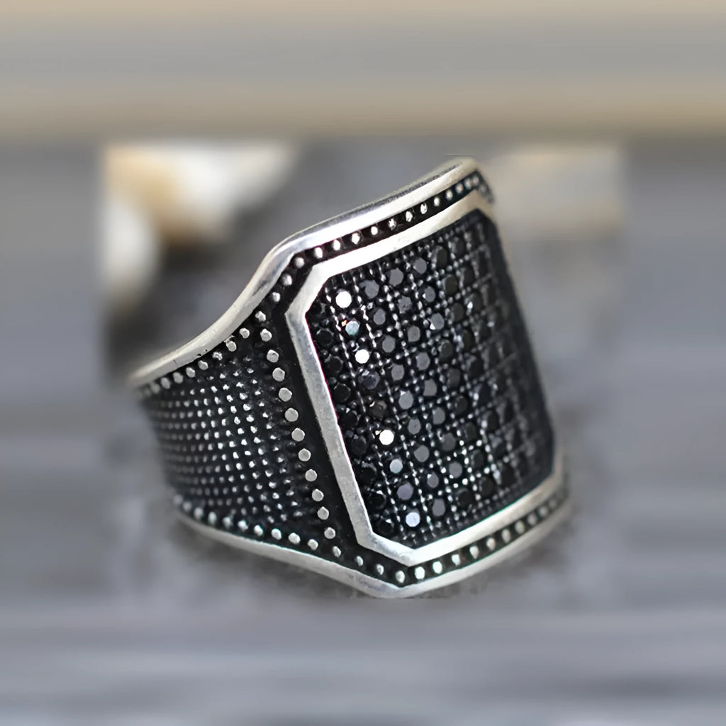 Close-up of a black alloy ring with a copper inlay stripe and sparkling clear zircon stones on a finger.