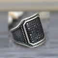 Close-up of a black alloy ring with a copper inlay stripe and sparkling clear zircon stones on a finger.