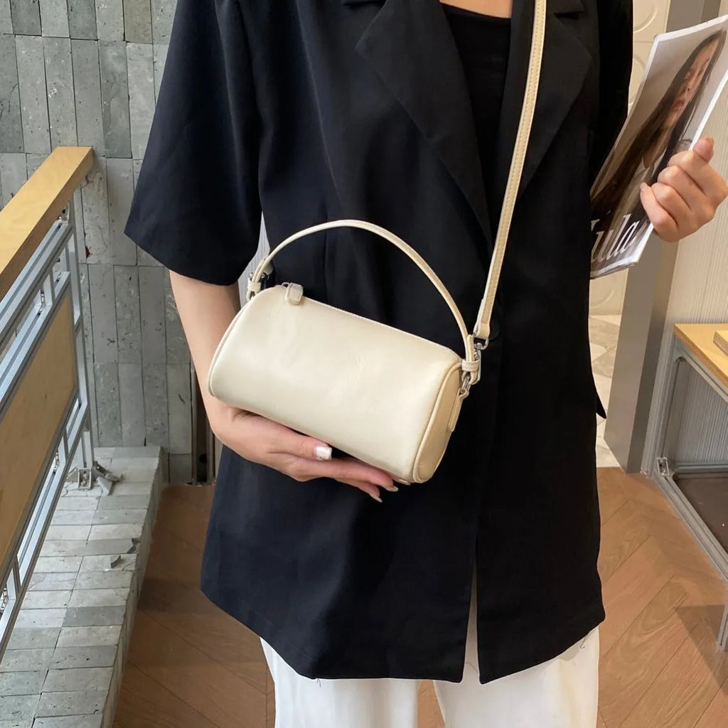 Genuine leather cylindrical crossbody phone bag in black, shown with single shoulder strap and visible sewing thread detail.