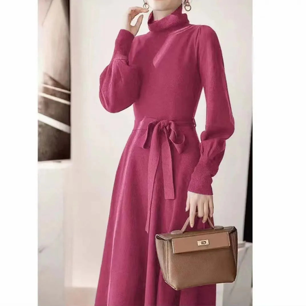 A woman wearing a rose red turtleneck knit dress with long sleeves, an elastic waist, and a loose mid-length hem.