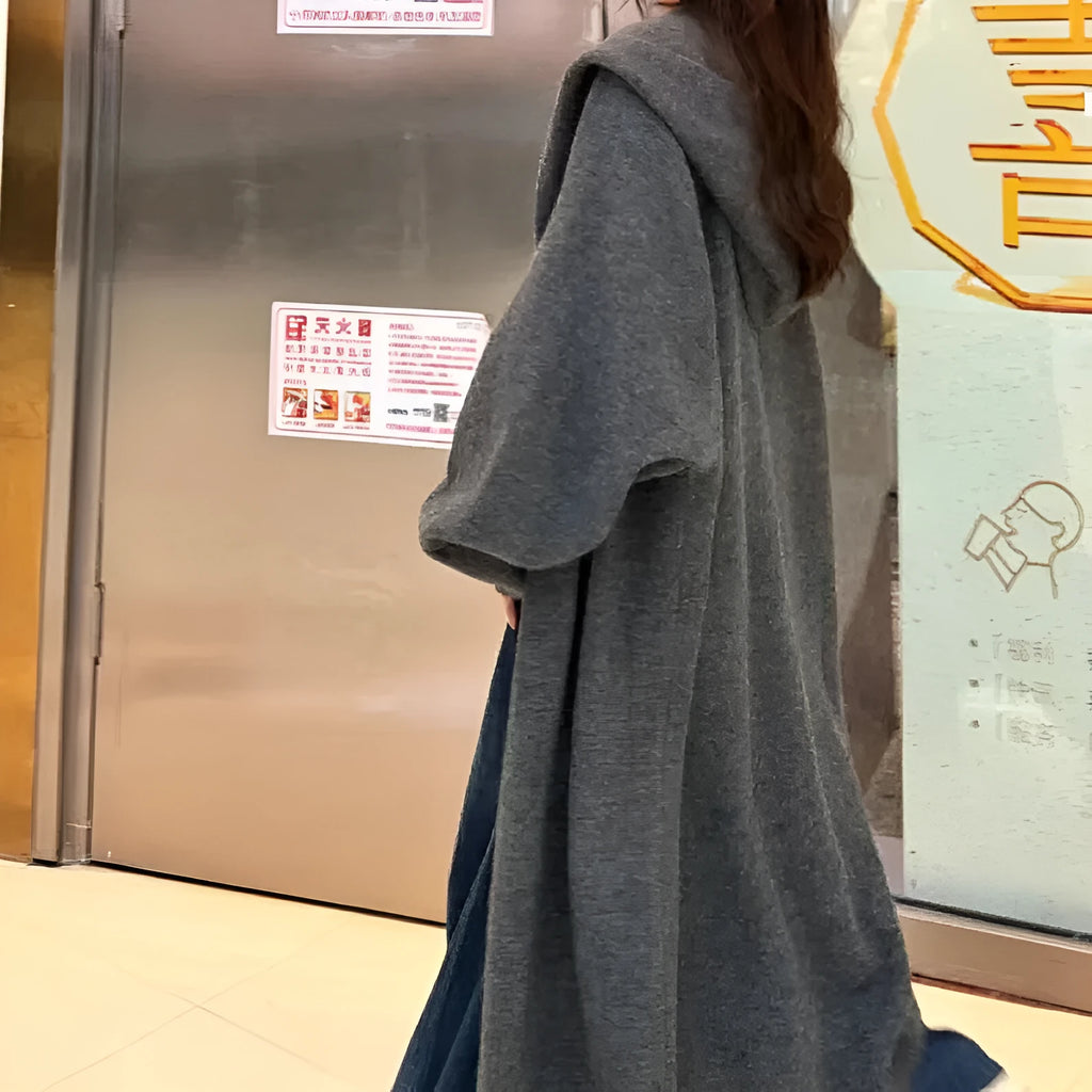A woman wearing a long, loose-fitting, hooded knitted cardigan in a solid colour, showcasing its below-the-knee length.