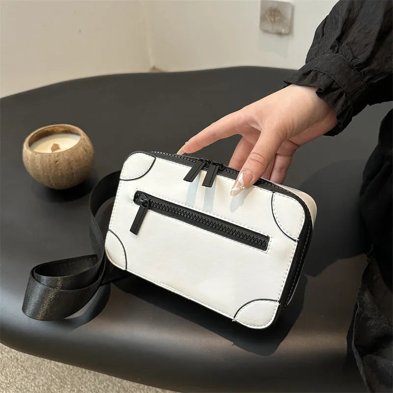 A small, square, structured crossbody bag in a choice of colours, showing its horizontal shape and sewing line detailing.