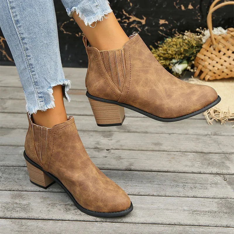 Women's black slip-on ankle boots with pointed toe and thick square heel on a wooden floor.