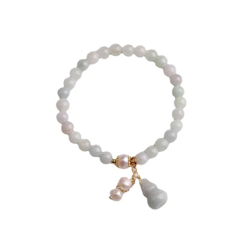 Close-up of a handmade emerald green jade gourd charm bracelet with a pearl detail on an adjustable cord.