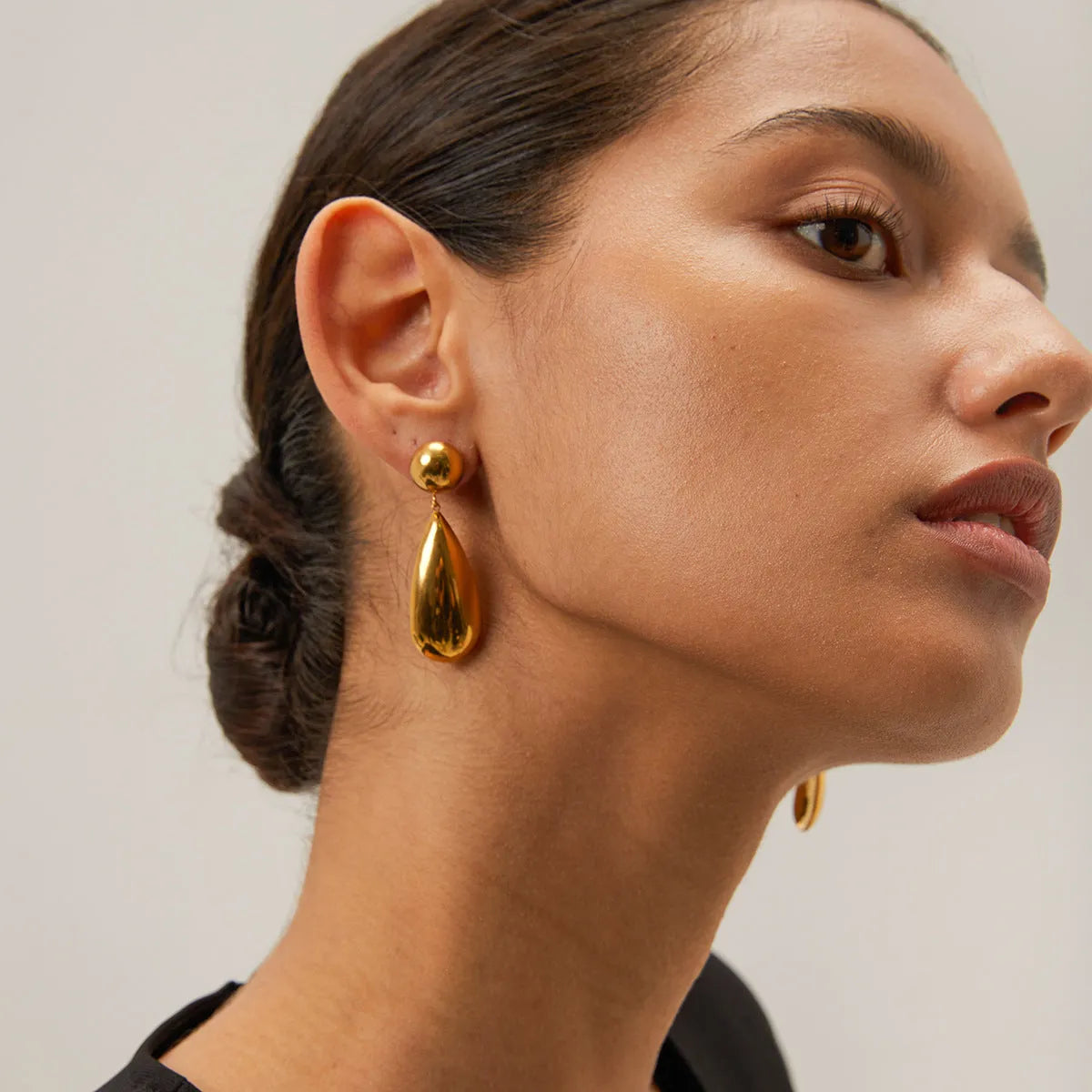 A pair of gold geometric hemisphere earrings with a water droplet pendant design on a white background.