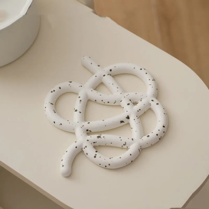 Irregular-shaped ceramic heat proof mat with hook and loop backing on a wooden table.