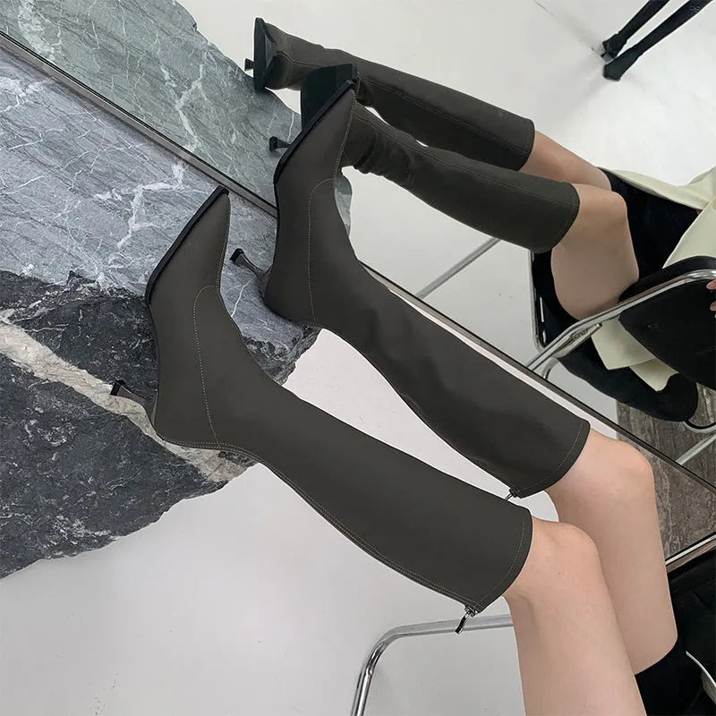 Black pointed toe below-the-knee women's boots with a stiletto heel and a visible back zipper on a plain background.