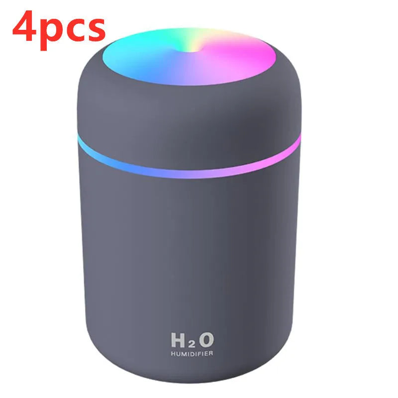 Pink USB mini humidifier with LED lights on wooden desk beside laptop