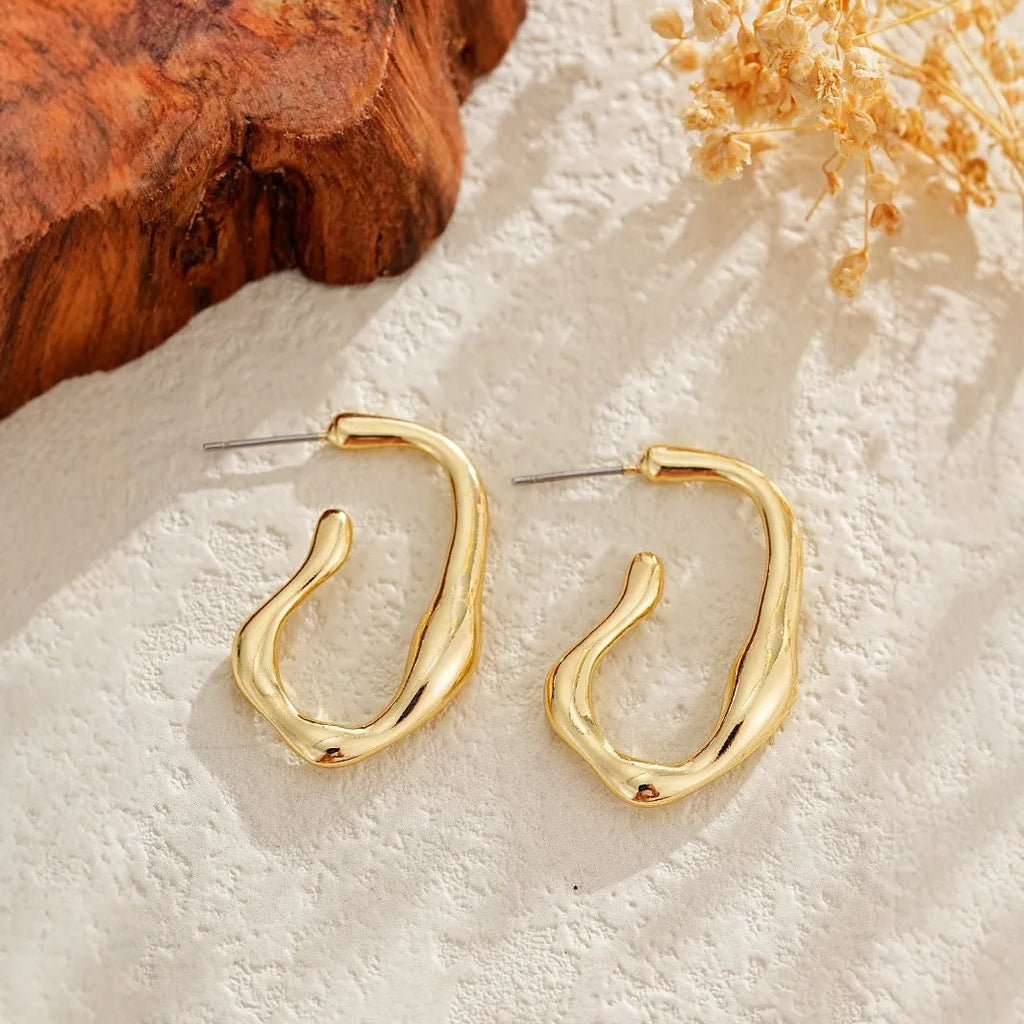 Gold irregular shaped minimalist drop earrings with abstract geometric design on neutral background