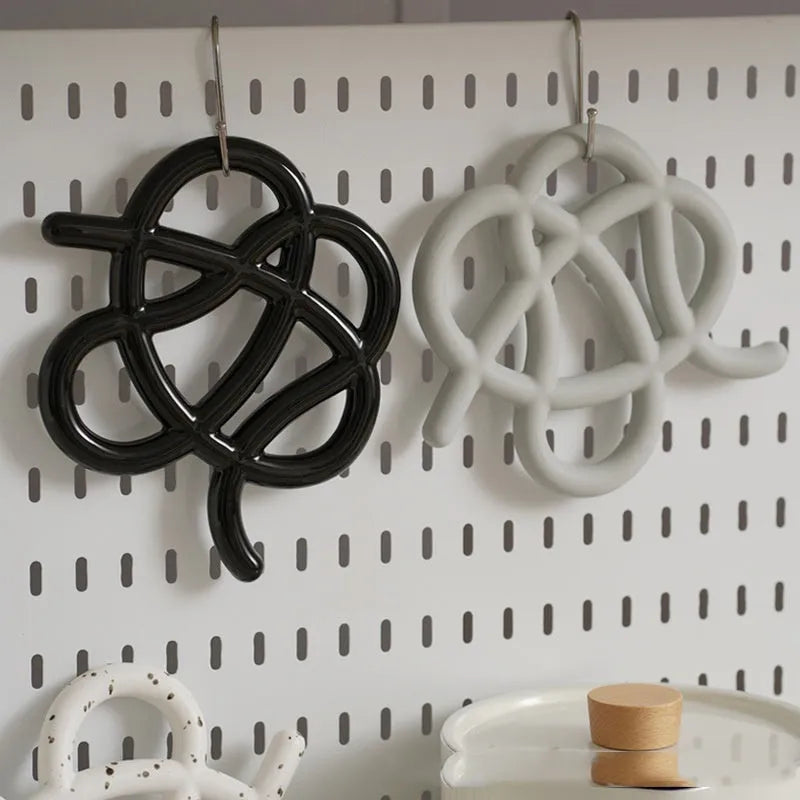 Irregular-shaped ceramic heat proof mat with hook and loop backing on a wooden table.