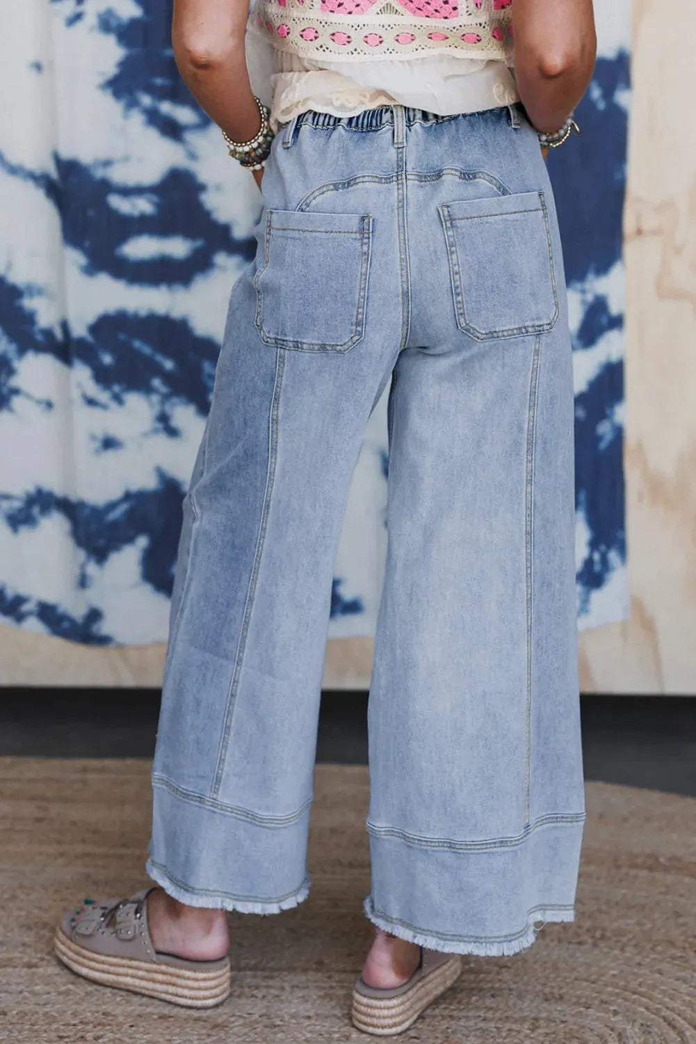 Women's beau blue wide-leg denim trousers on a hanger, showing drawstring waist and raw hem detail.