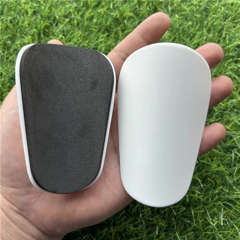 Extra small mini plastic football shin guards in black and white, shown at 8cm by 5cm size.