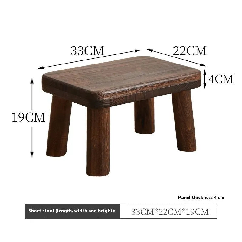A solid wood stool with a distressed finish, used for changing shoes in a living room.