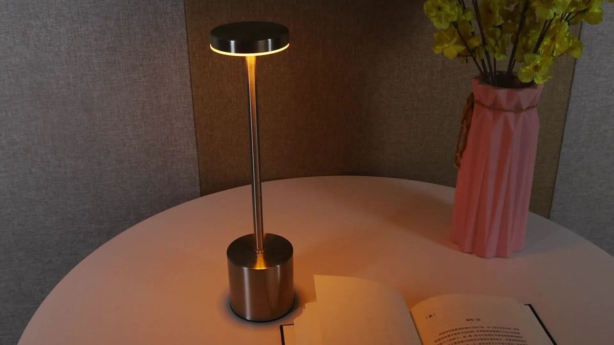 Modern minimalist iron table lamp with silver finish, I-shaped silhouette, emitting warm ambient light on a bedside table