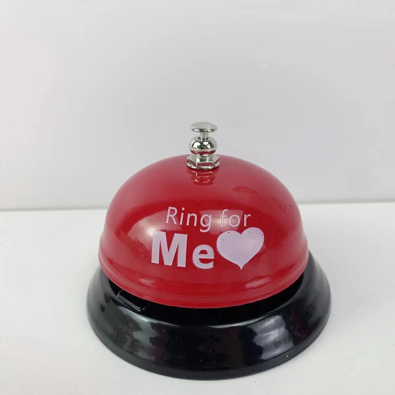 Iron table serving bell in multiple colour options on a wooden surface.