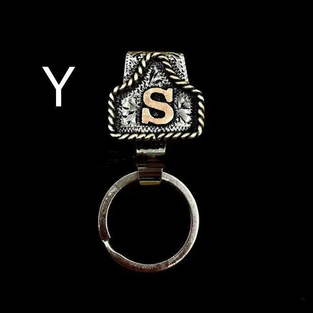 Handmade metal cow tag belt keychain showing one of 26 colour options, each marked with a different alphabet letter.
