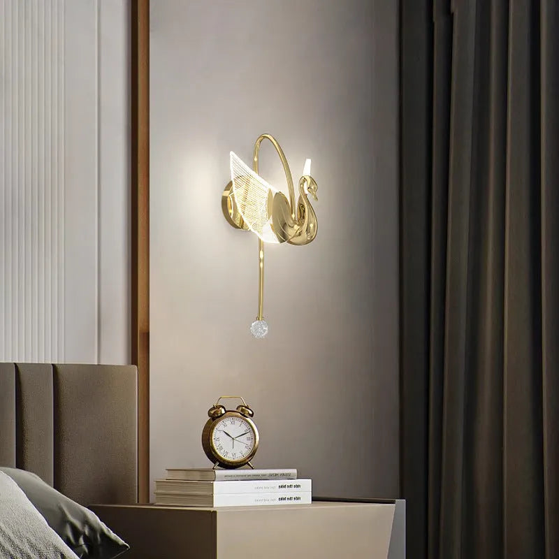 Gold modern minimalist swan-shaped LED wall lamp with an acrylic shade on a wall.