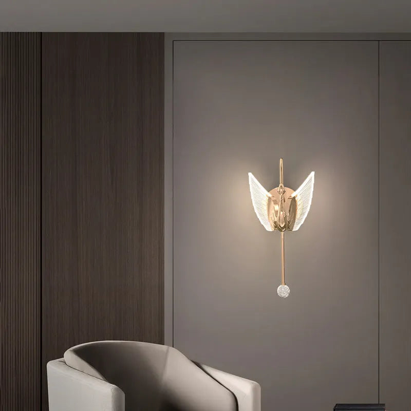 Gold modern minimalist swan-shaped LED wall lamp with an acrylic shade on a wall.