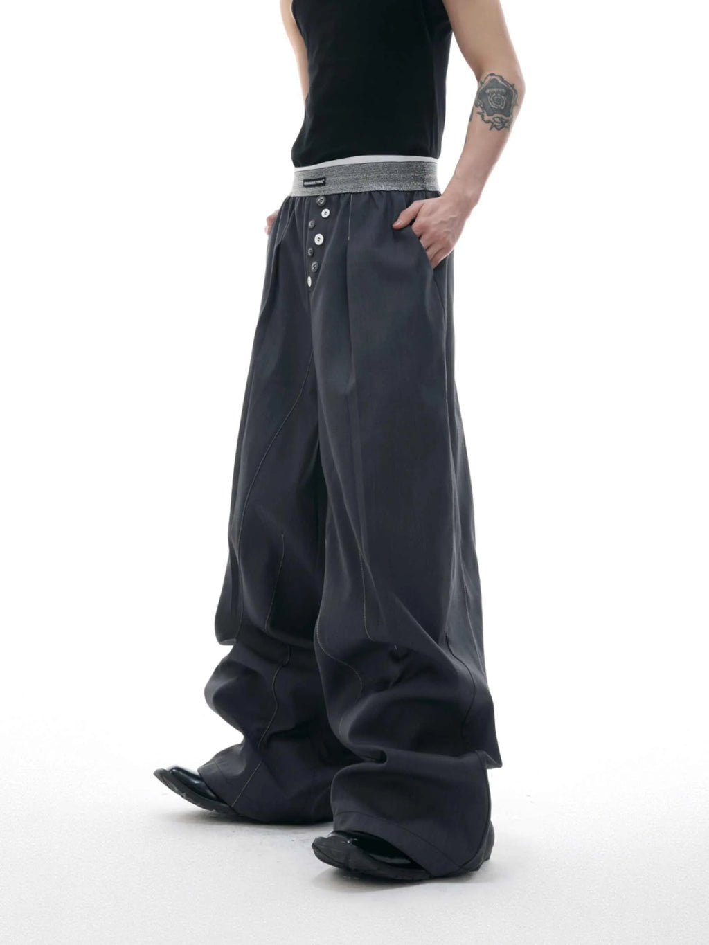 Straight-leg high-waisted trousers in black with a drooping waistband and button detail on a neutral background.