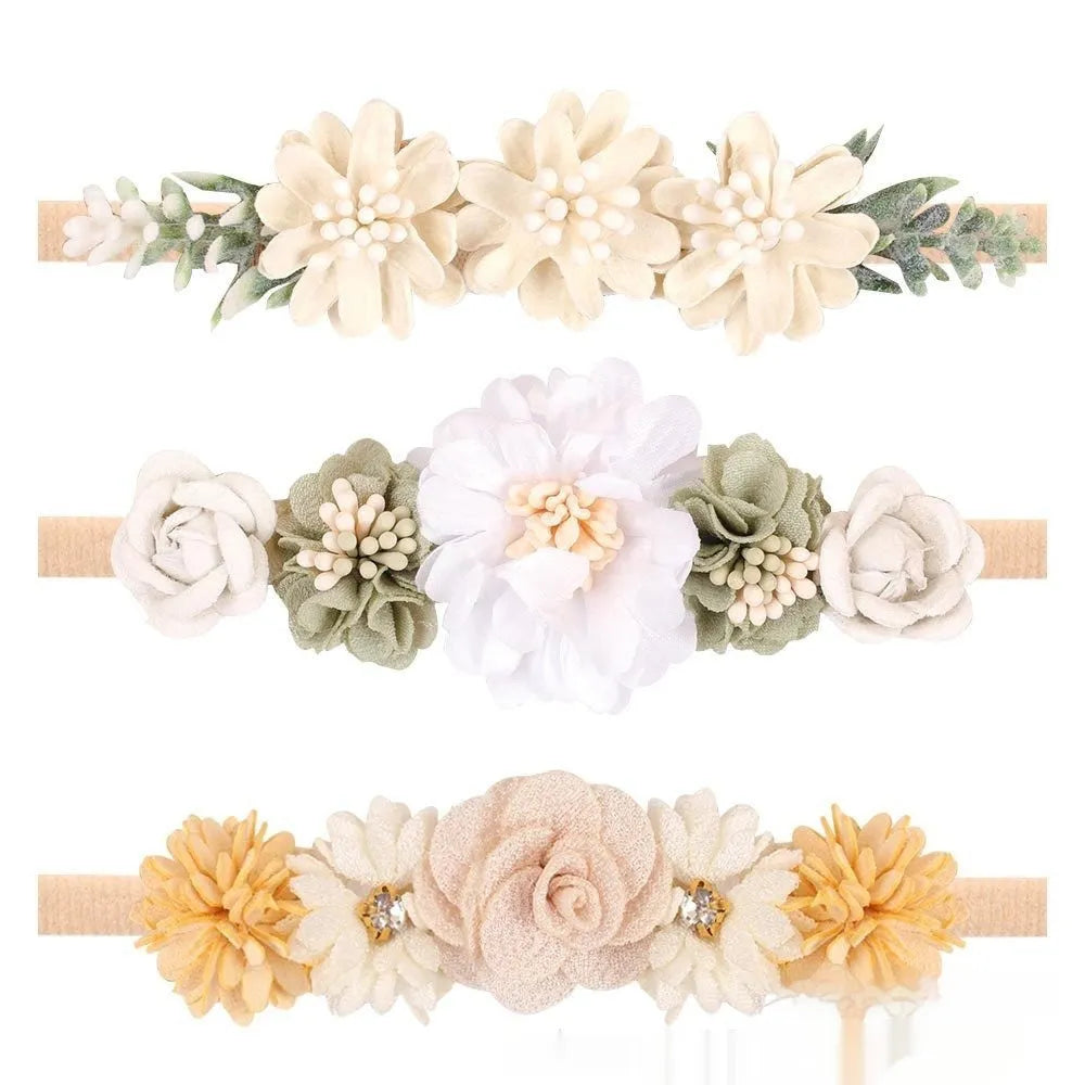 Three cloth flower-shaped hair bands for children in different styles on a light background