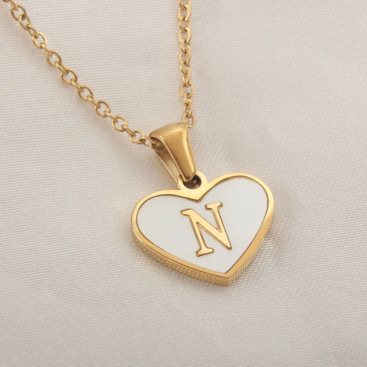 Gold-plated heart necklace with white shell pendant showing initial engraving on stainless steel chain