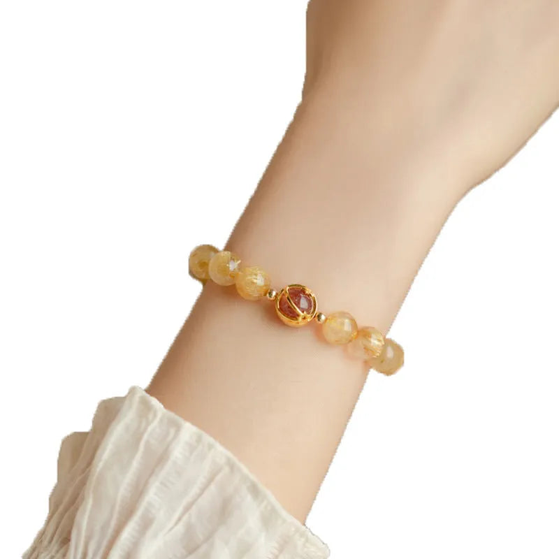 Citrine gold rutilated quartz crystal bracelet with diamond-cut beads on a wrist.
