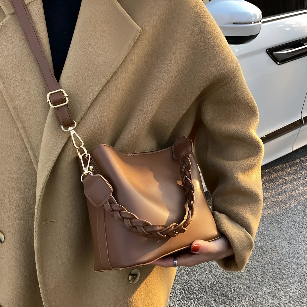 Khaki woven texture one-shoulder crossbody bucket bag with an underarm strap on a table.