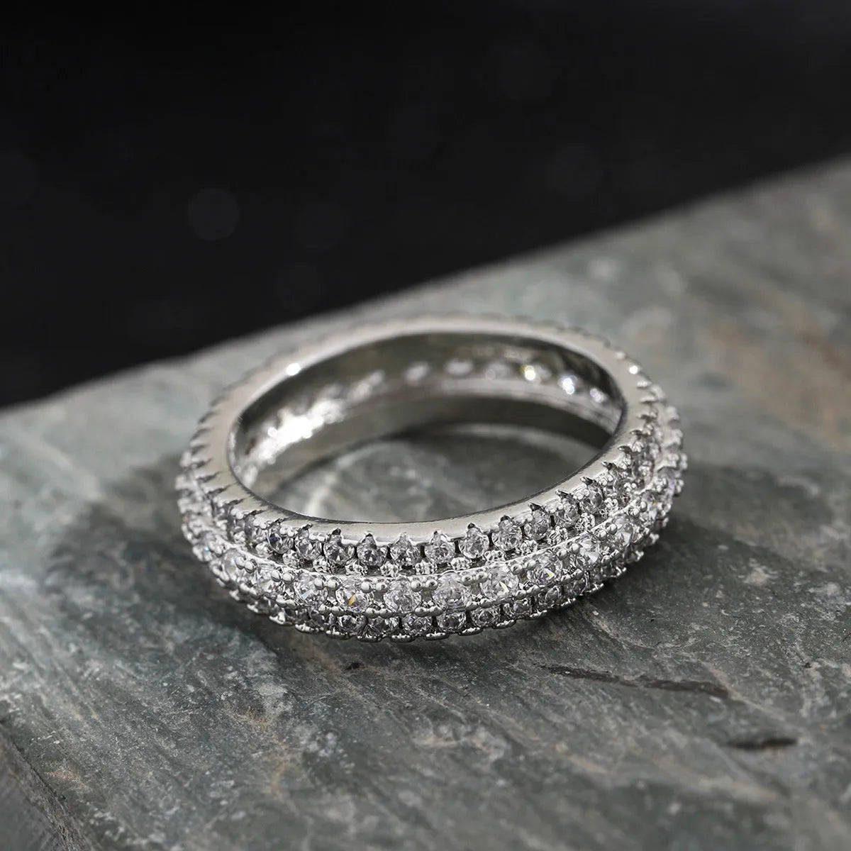 Geometric copper ring with a triangular zircon stone, shown in white gold finish on a finger.