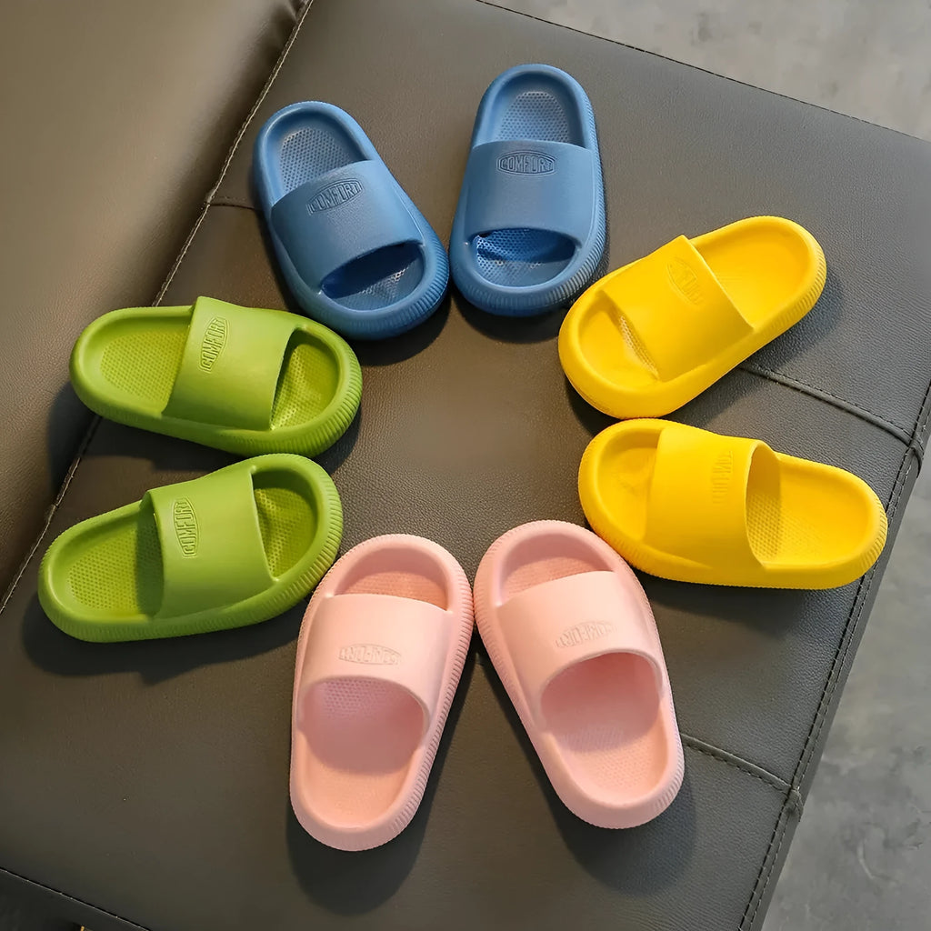 A pair of bright blue, one-piece EVA children's slippers with a textured non-slip sole, shown on a wooden floor.