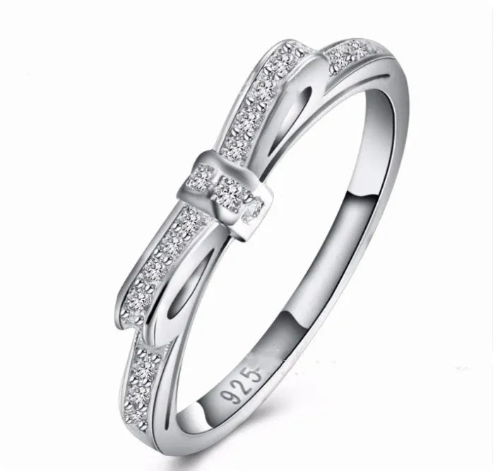 Silver-coloured bow-shaped ring with sparkling zircon crystals on a model's finger.
