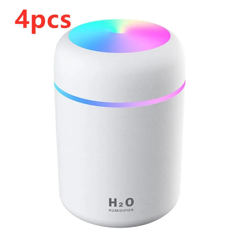 Pink USB mini humidifier with LED lights on wooden desk beside laptop