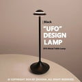 Modern UFO-shaped metal table lamp in black on a wooden desk, showing touch controls and soft glow.