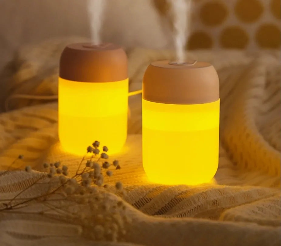 White cylindrical mini humidifier with USB cable and aromatherapy tray on a wooden desk.