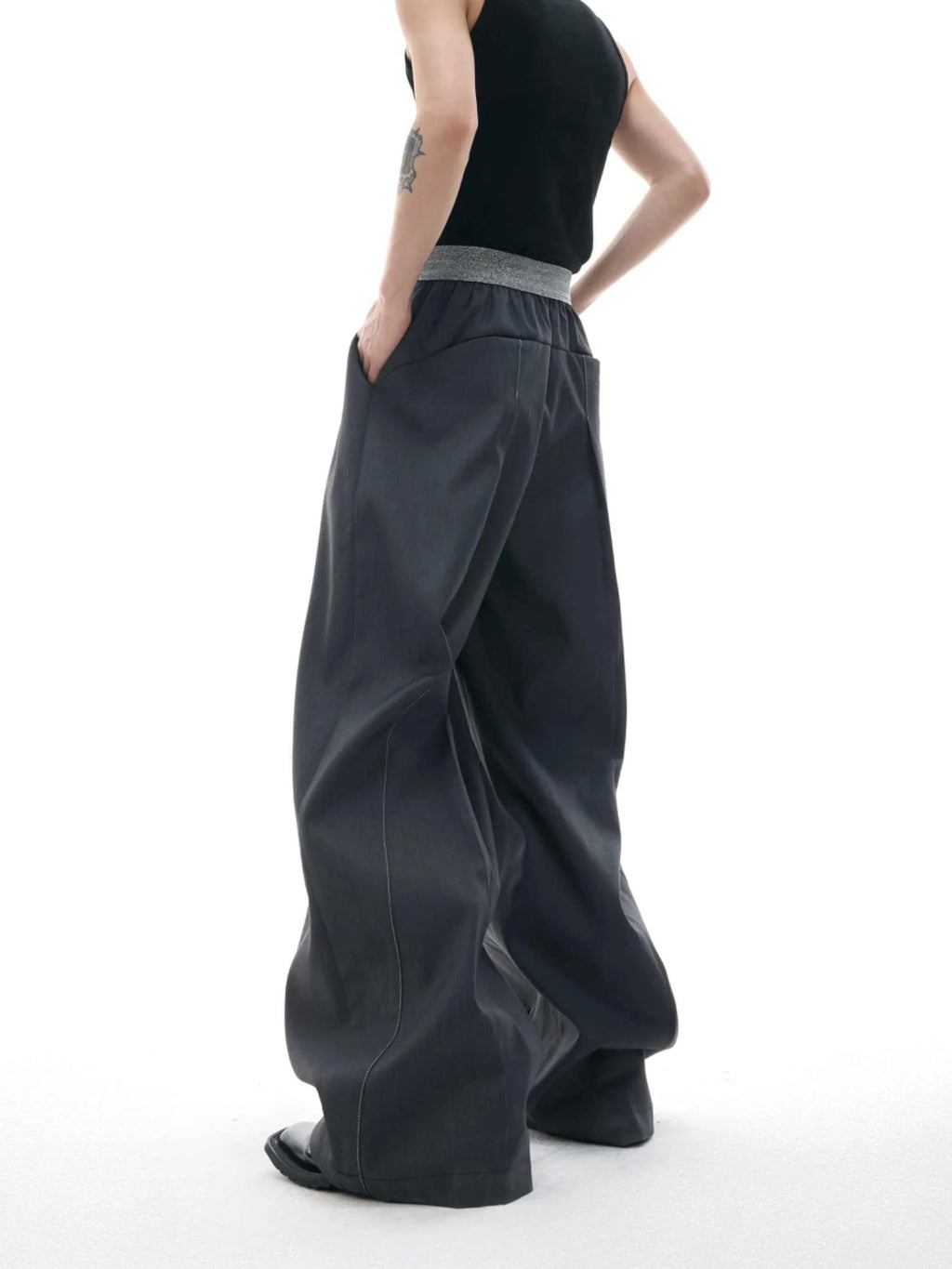 Straight-leg high-waisted trousers in black with a drooping waistband and button detail on a neutral background.