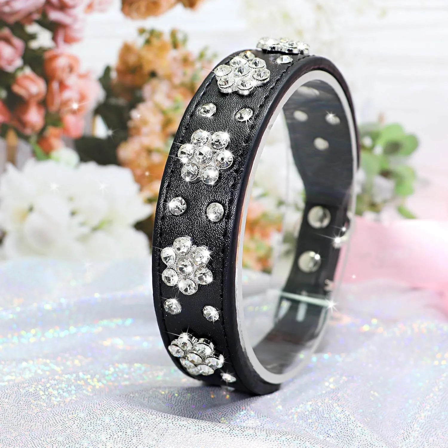 A black PU leather dog collar decorated with sparkling rhinestone flowers and metal studs, showing the adjustable eyelets and metal D-ring.