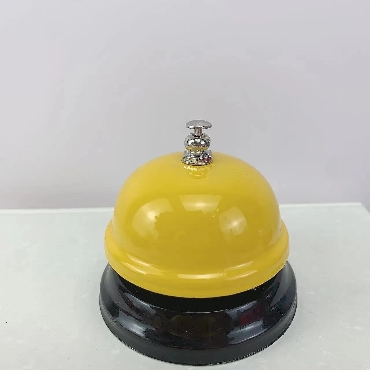 Iron table serving bell in multiple colour options on a wooden surface.