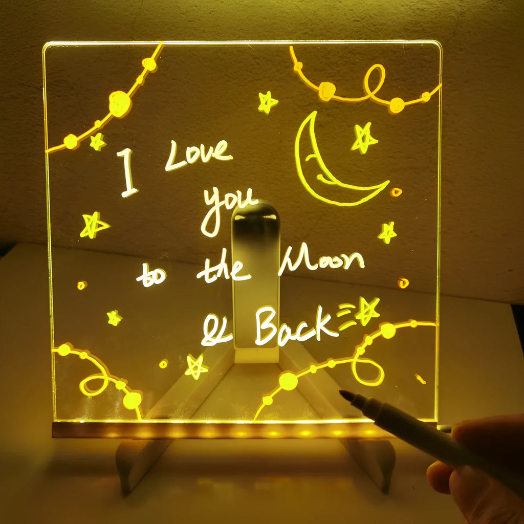 DIY acrylic message board LED night light on desk with colourful writing, USB cable, and pens