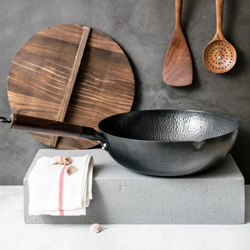Black traditional cast iron wok with a long wooden handle on a kitchen counter.