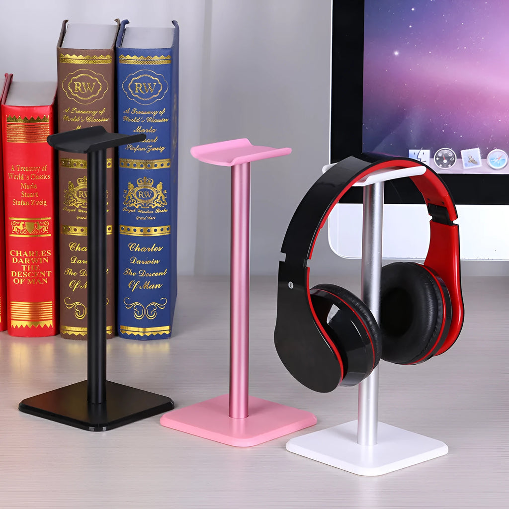 Detachable aluminum alloy headset hanger with TPU rubber cradle, shown in white, pink, and black, fixed to a table.
